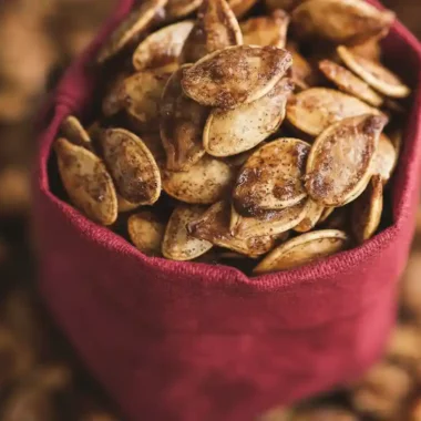 A detailed close-up of cinnamon sugar roasted pumpkin seeds filling a small red cloth bag, highlighting their sweet, crystallized coating from a cinnamon sugar roasted pumpkin seeds recipe.
