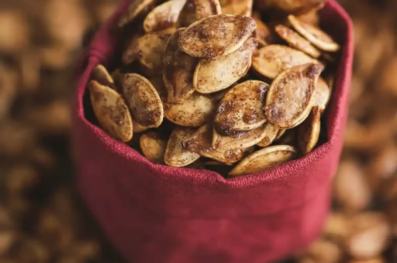 A detailed close-up of cinnamon sugar roasted pumpkin seeds filling a small red cloth bag, highlighting their sweet, crystallized coating from a cinnamon sugar roasted pumpkin seeds recipe.