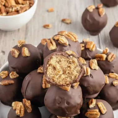 Easy No-Bake Pecan Pie Balls 4 A plate of chocolate-covered pecan pie balls, with one cut in half to show the rich, crumbly pecan pie filling inside, and topped with chopped pecans.