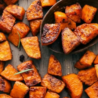 The Ultimate Roasted Sweet Potatoes Recipe 4 An overhead, close-up shot of perfectly caramelized and seasoned roasted sweet potatoes scattered on a rustic wooden board, with a wooden spoon scooping some up.