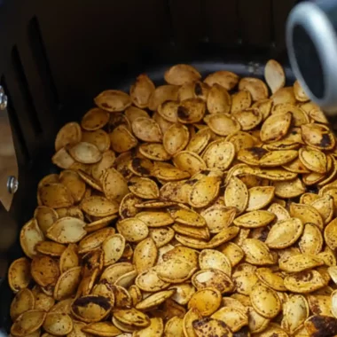 A close-up view of seasoned pumpkin seeds roasting inside the basket of an air fryer, demonstrating the air fryer pumpkin seeds recipe.