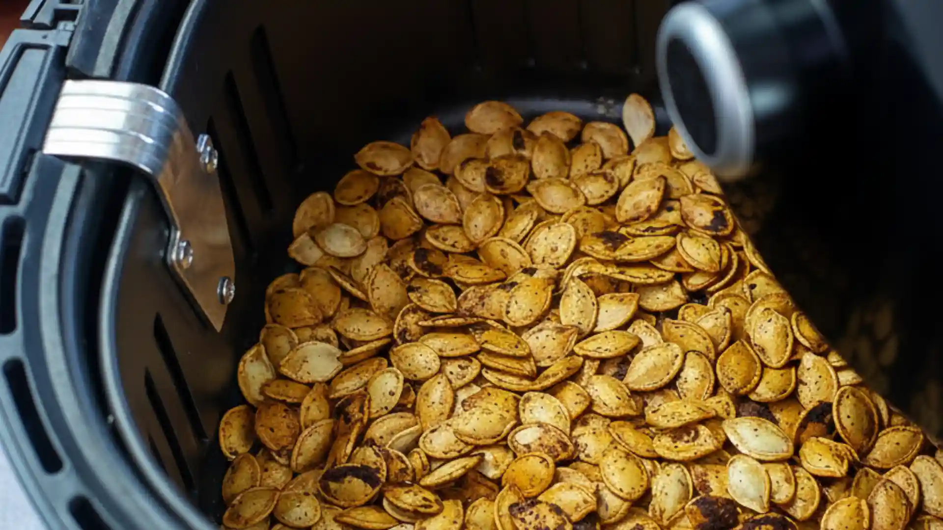 A close-up view of seasoned pumpkin seeds roasting inside the basket of an air fryer, demonstrating the air fryer pumpkin seeds recipe.