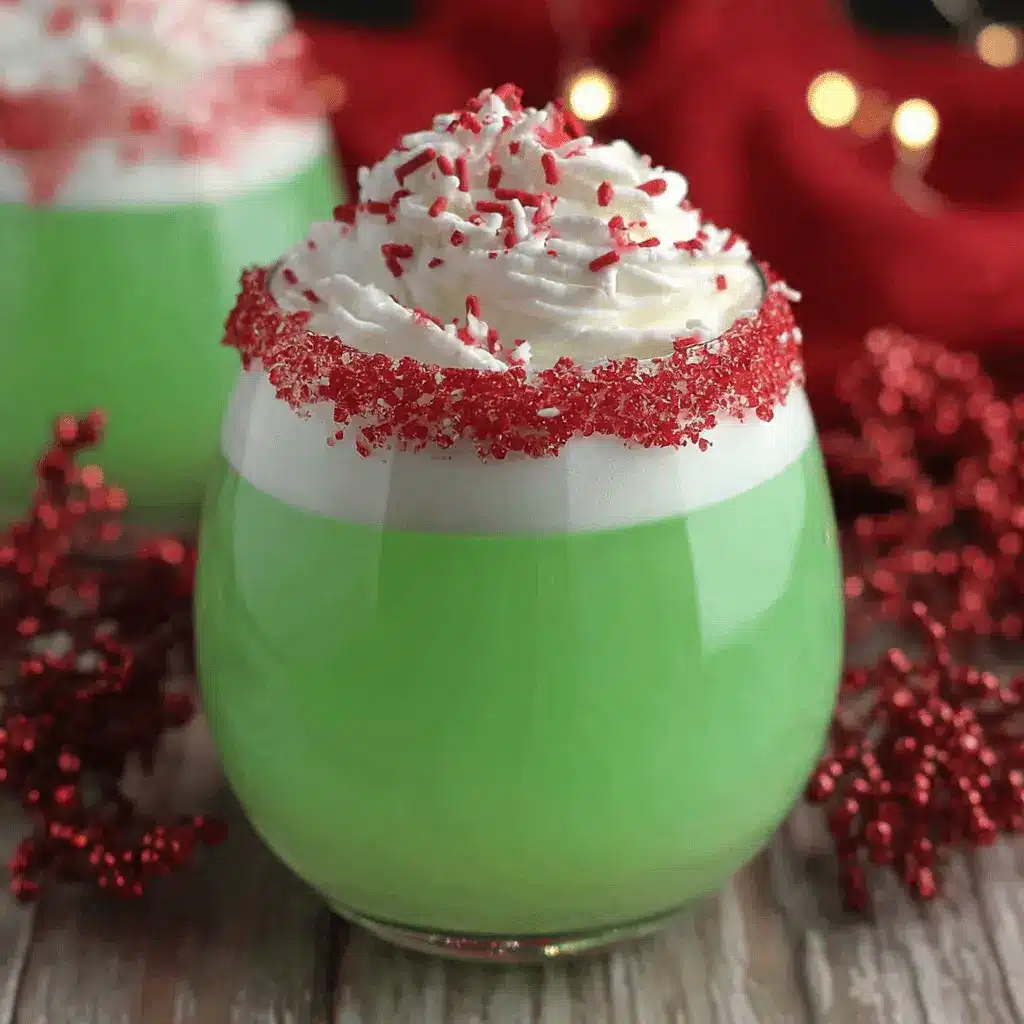Vibrant Grinch Punch in a stemless glass, topped with whipped cream, red and white sprinkles, and a sparkling red sugar rim, set against a festive red background with holiday lights.