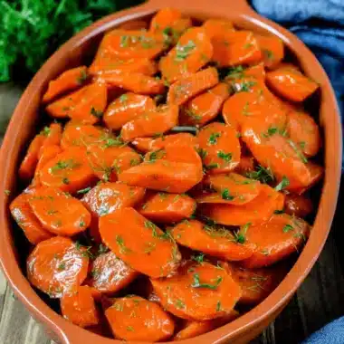 Amazing Glazed Carrots in Under 20 Mins 3 Close-up of vibrant, tender glazed carrots garnished with fresh dill in a rustic baking dish.