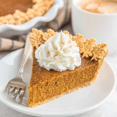 Easy Pumpkin Pie Recipe 3 A delectable slice of pumpkin pie topped with whipped cream and pastry leaves, ready to be enjoyed.