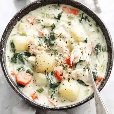 Close-up of creamy chicken gnocchi soup garnished with fresh thyme in a dark bowl.