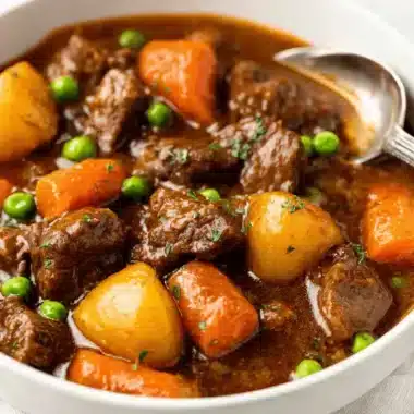The Ultimate Foolproof Crockpot Beef Stew 4 Close-up of hearty crockpot beef stew with tender beef, carrots, potatoes, and peas in a white bowl.