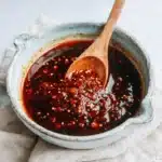 Rustic bowl of homemade chili oil with visible chili flakes and sesame seeds, perfect for a new chili oil recipe.
