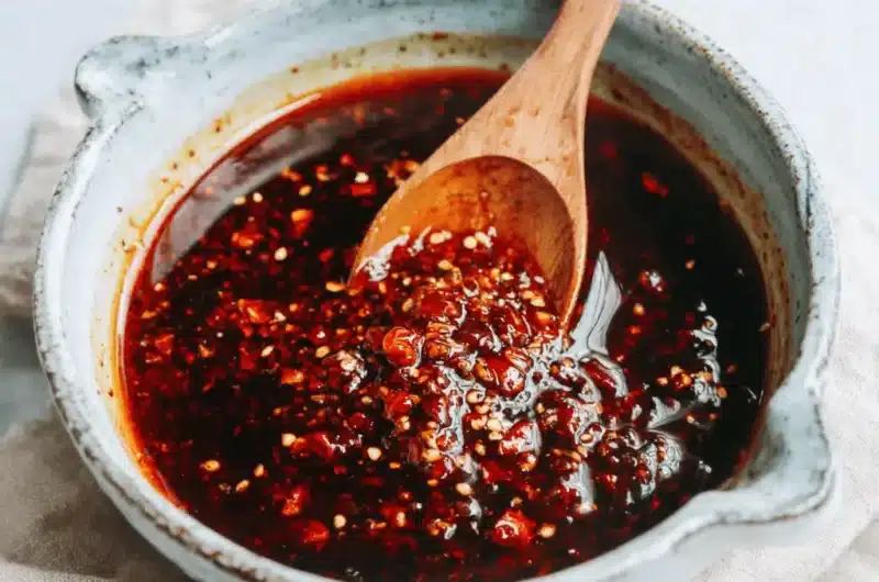 Rustic bowl of homemade chili oil with visible chili flakes and sesame seeds, perfect for a new chili oil recipe.