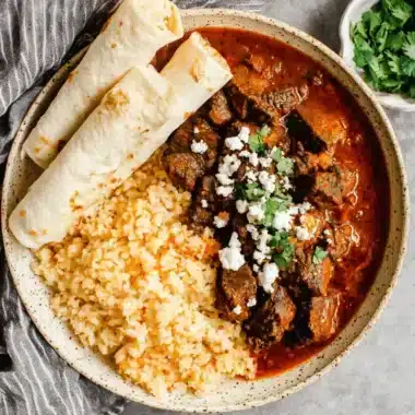 Rustic bowl of hearty chili colorado recipe served with fluffy rice and flatbread, garnished with cheese and fresh herbs.