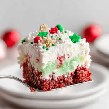 The Ultimate Christmas Cookie Lasagna Recipe 3 A vibrant slice of layered Christmas Cookie Lasagna with red, green, and white layers, topped with festive sprinkles and stars, served on a silver spatula.