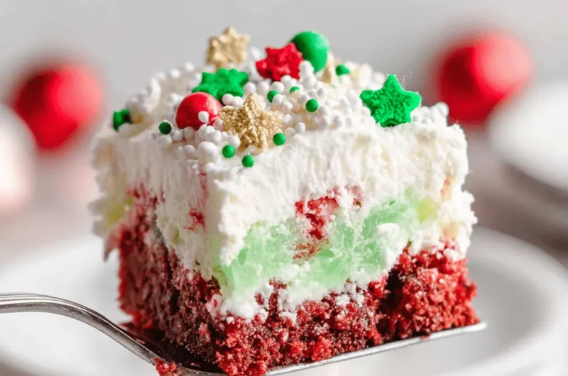 A vibrant slice of layered Christmas Cookie Lasagna with red, green, and white layers, topped with festive sprinkles and stars, served on a silver spatula.