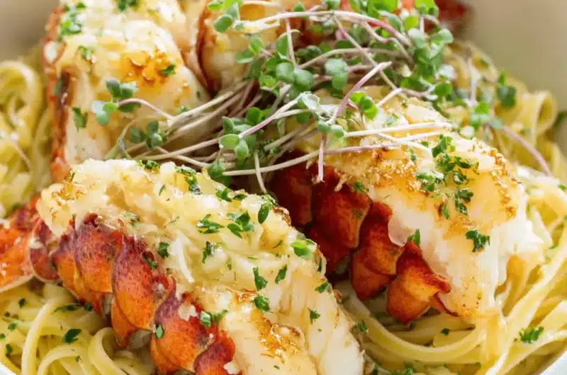 Close-up of three succulent, split Butter Poached Lobster tails served over a bed of linguine pasta with fresh herbs and microgreens.
