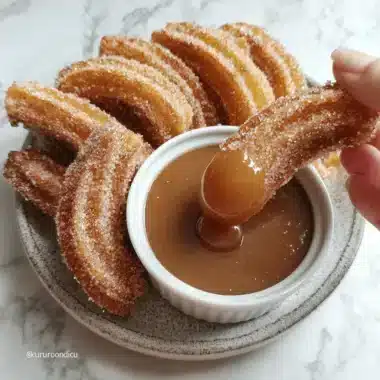 A hand dips a golden, cinnamon-sugar coated Air Fryer Churro Bite into a rich caramel sauce on a rustic ceramic plate.