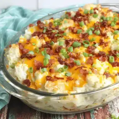 Golden-brown loaded baked potato casserole topped with melted cheddar, crispy bacon, and fresh green onions in a glass dish.