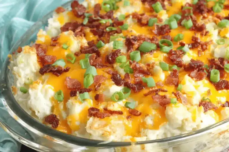 Golden-brown loaded baked potato casserole topped with melted cheddar, crispy bacon, and fresh green onions in a glass dish.