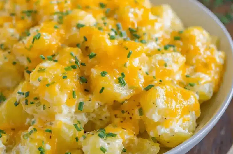 Close-up of a bowl of creamy, melted cheddar crockpot cheesy potatoes garnished with fresh chives.