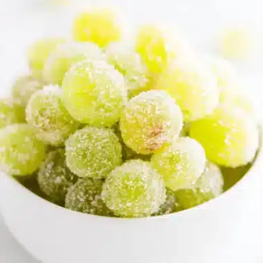 Bright close-up of sparkling, frosted green Sugared Champagne Grapes in a white bowl.
