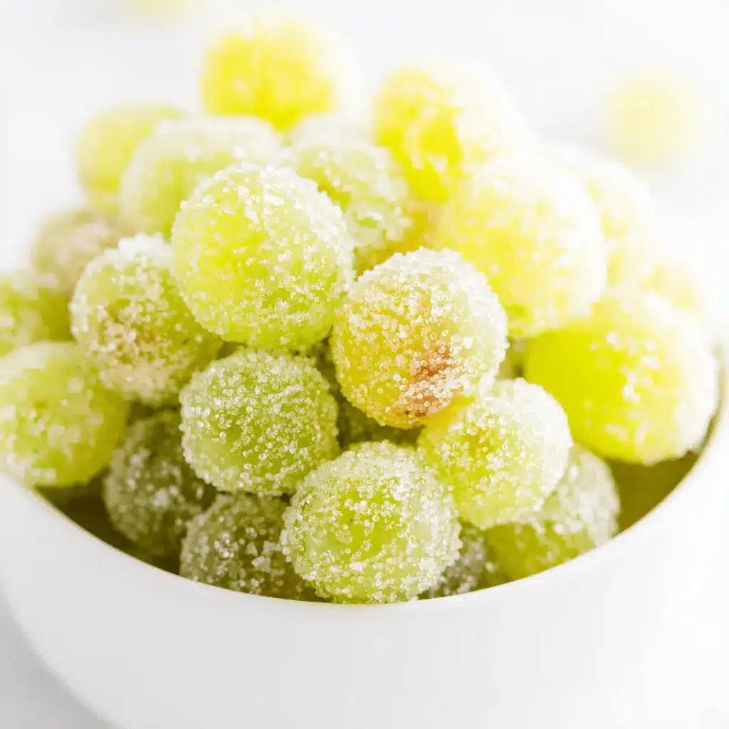 Bright close-up of sparkling, frosted green Sugared Champagne Grapes in a white bowl.