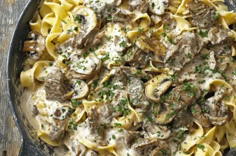 Hearty Prime Rib Stroganoff served in a black cast iron skillet, featuring wide egg noodles, prime rib chunks, and a creamy sauce.