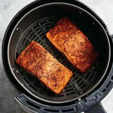 Ultimate Air Fryer Salmon Recipes 3 Perfectly cooked, heavily seasoned salmon fillets inside a black air fryer basket, demonstrating successful air fryer salmon recipes.