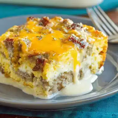 Close-up of a hearty slice of biscuits and gravy breakfast casserole layered with savory sausage, melted cheddar, and creamy gravy.