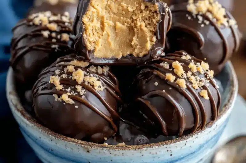 Appetizing close-up of chocolate-covered Peanut Butter Balls in a ceramic bowl, one cut open to reveal creamy filling.