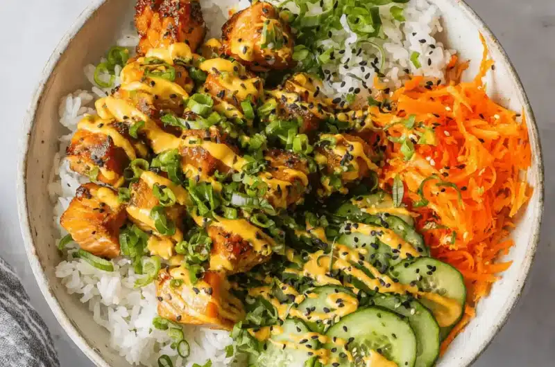 Overhead view of a delicious glazed salmon bowl with rice, shredded carrots, cucumber, spicy mayo, and black sesame seeds.