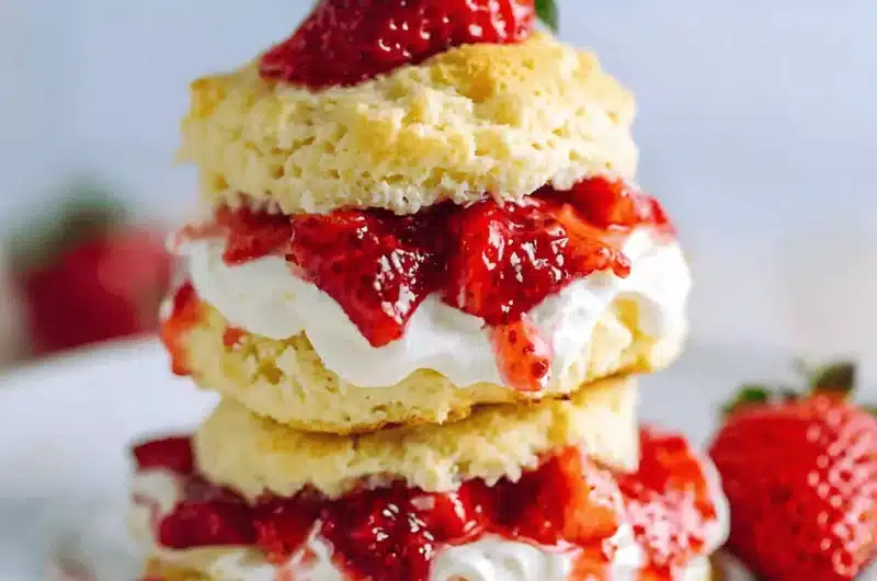 Double-stacked strawberry shortcake featuring flaky biscuits, generous whipped cream, and rich, dripping strawberry topping.