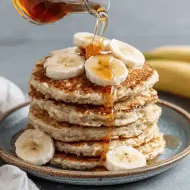 Close-up of syrupy banana pancakes stacked high with fresh slices on a rustic teal plate.