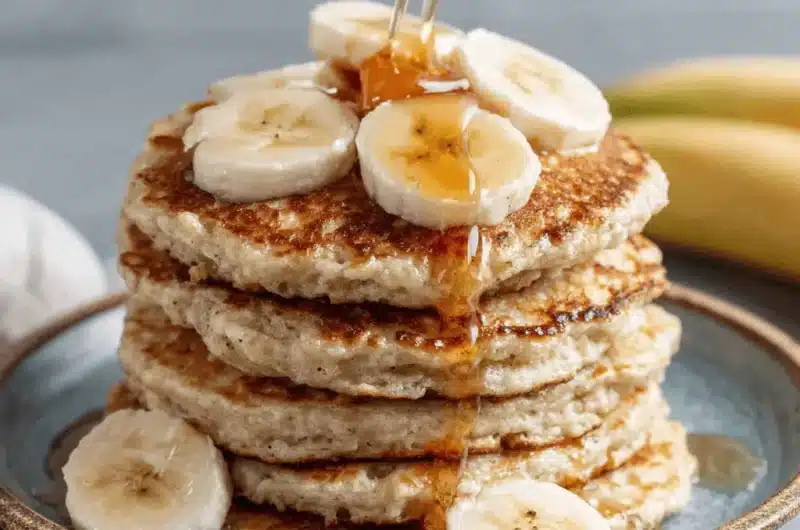 Close-up of syrupy banana pancakes stacked high with fresh slices on a rustic teal plate.