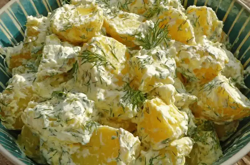 Close-up of creamy, dill-garnished homemade potato salad with egg served in a rustic bowl on a wooden table.