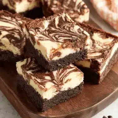 Close-up of fudgy brownie cheesecake squares stacked on a dark wooden board, showcasing the creamy swirled marbling effect.
