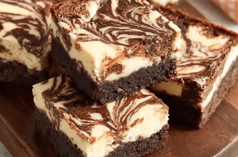 Close-up of fudgy brownie cheesecake squares stacked on a dark wooden board, showcasing the creamy swirled marbling effect.