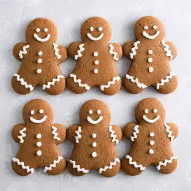 Ultimate Soft Gingerbread Men Cookies Recipe 3 Six neatly arranged Gingerbread Men Cookies with detailed white royal icing decoration, shot flat lay on a textured gray surface.