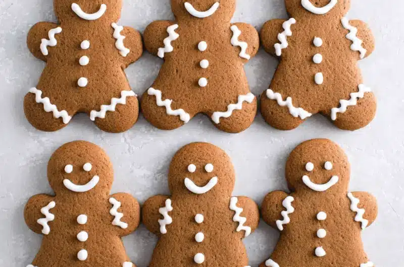 Six neatly arranged Gingerbread Men Cookies with detailed white royal icing decoration, shot flat lay on a textured gray surface.