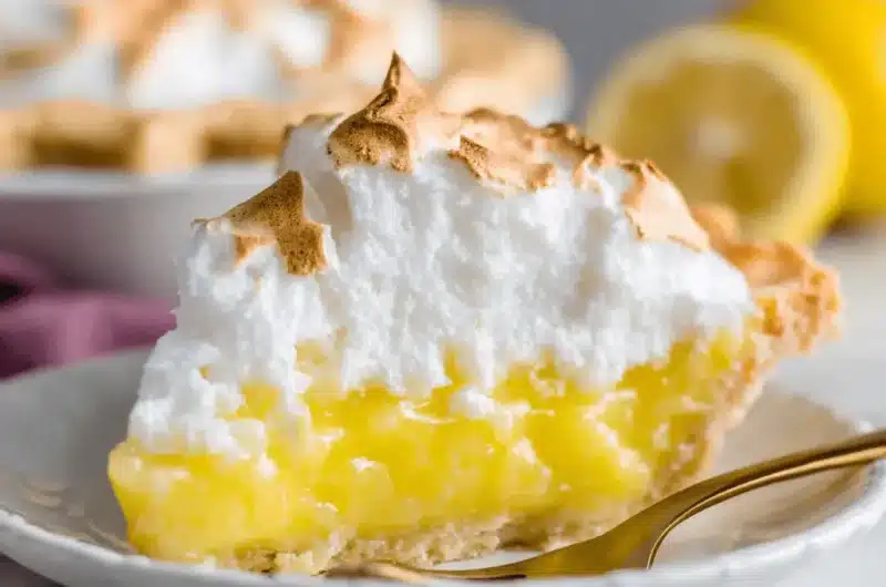 Appetizing slice of lemon meringue pie featuring tall, perfectly toasted meringue peaks and vibrant yellow lemon curd.