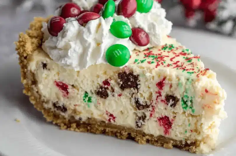 Slice of decadent christmas cheesecake topped with whipped cream, red and green M&Ms, and festive sprinkles.
