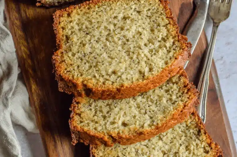 Overhead view of moist slices of freshly baked cake mix banana bread resting on a dark wooden cutting board with a vintage knife and fork.