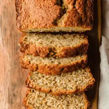 Top-down view of moist, stacked slices of freshly baked sour cream banana bread on a rustic wooden cutting board.