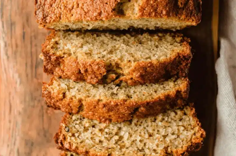 Top-down view of moist, stacked slices of freshly baked sour cream banana bread on a rustic wooden cutting board.