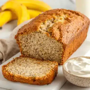 Moist slice of freshly baked greek yogurt banana bread next to a bowl of creamy Greek yogurt on a marble cutting board.