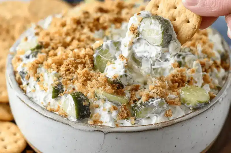 Hand scooping creamy homemade Fried Pickle Dip garnished with golden crunchy crumbs and dill from a rustic bowl.