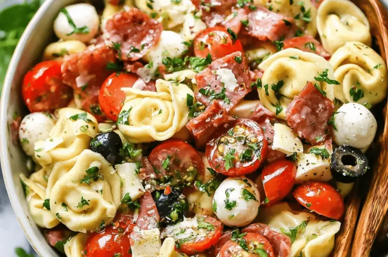 Hearty Italian tortellini pasta salad with salami, mini mozzarella, cherry tomatoes, and fresh herbs in a ceramic serving bowl.
