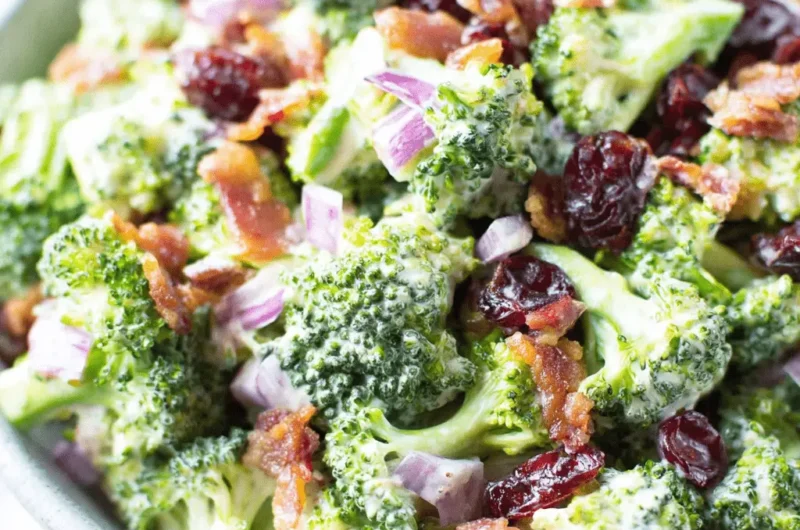 Appetizing close-up of classic creamy **broccoli salad** featuring bacon crumbles and dried cranberries.