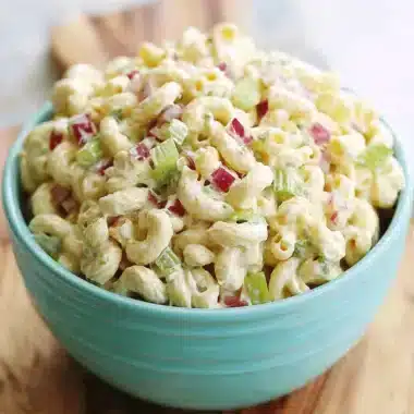 A generous bowl of creamy classic macaroni salad with celery and red onion, served in a bright aqua blue bowl.