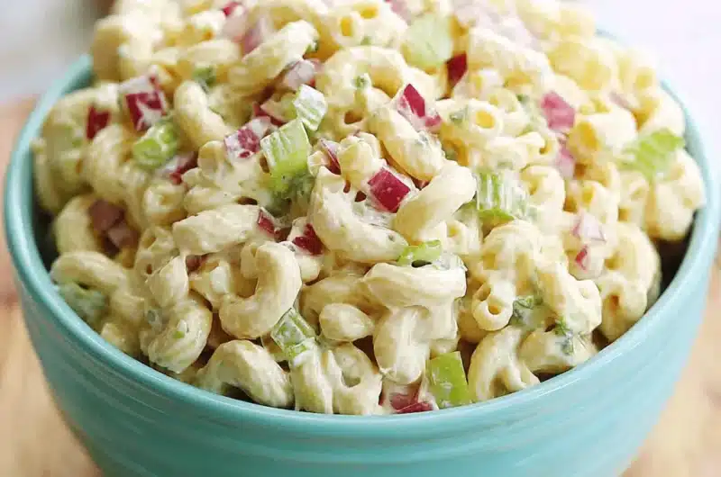A generous bowl of creamy classic macaroni salad with celery and red onion, served in a bright aqua blue bowl.