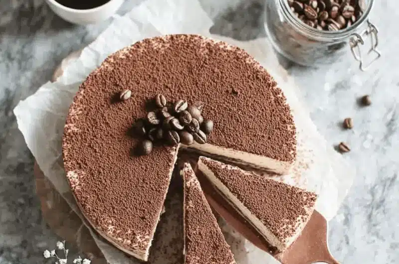 Overhead photograph of a cocoa-dusted, layered espresso martini cheesecake garnished with whole coffee beans on a rustic wooden platter.