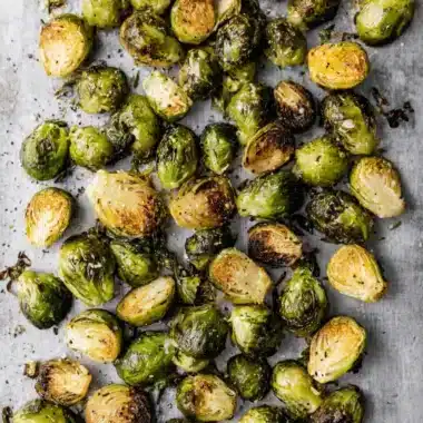 Highly detailed image of perfectly seasoned and caramelized Roasted Brussels Sprouts scattered on a light background.