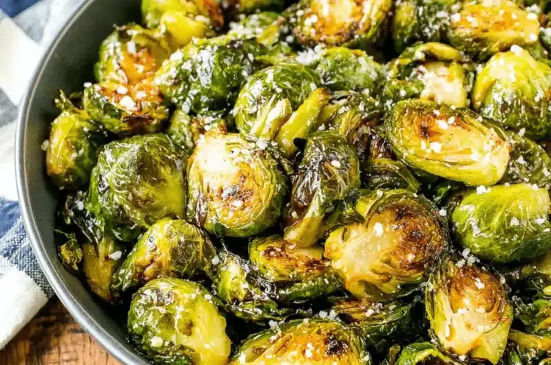 Highly caramelized roasted brussels sprouts recipe in a dark bowl, garnished with flaky sea salt.